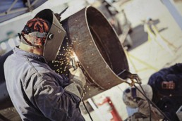Man wearing welding gear arc welding a 4' diameter pipe.