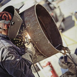 Man wearing welding gear arc welding a 4' diameter pipe.
